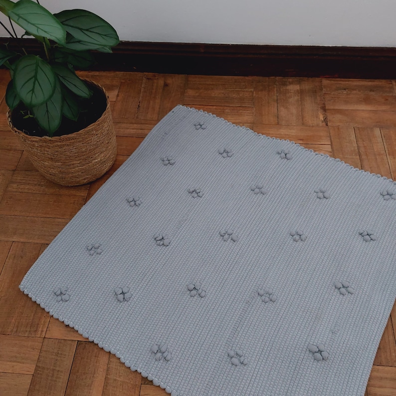 Puede incluir: Una alfombra gris claro con una superficie texturizada y un patr&oacute;n repetitivo de peque&ntilde;os c&iacute;rculos en relieve.