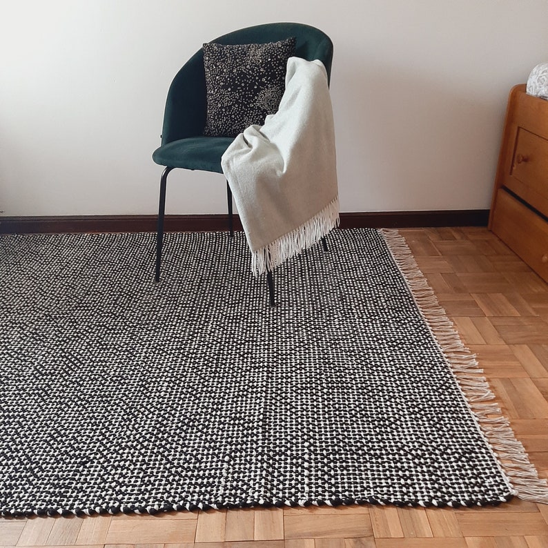 May include: A black and white patterned rug with fringe edges. A green chair with a white throw blanket is sitting on the rug.