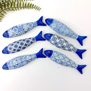 Peut inclure: Six figurines de poissons en céramique avec des motifs bleus et blancs. Les poissons ont des nageoires et des yeux bleu foncé. Les motifs varient, avec des motifs floraux et géométriques. Décoration intérieure.