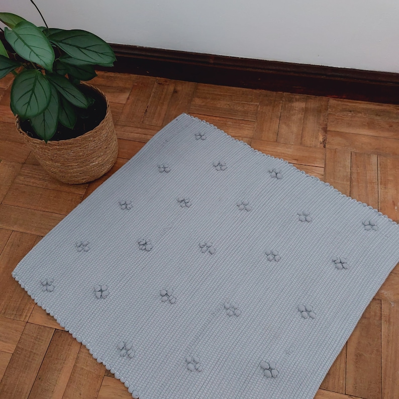 Puede incluir: Una alfombra gris claro con una superficie texturizada y un patr&oacute;n repetitivo de peque&ntilde;os c&iacute;rculos en relieve. La alfombra est&aacute; sobre un suelo de madera.