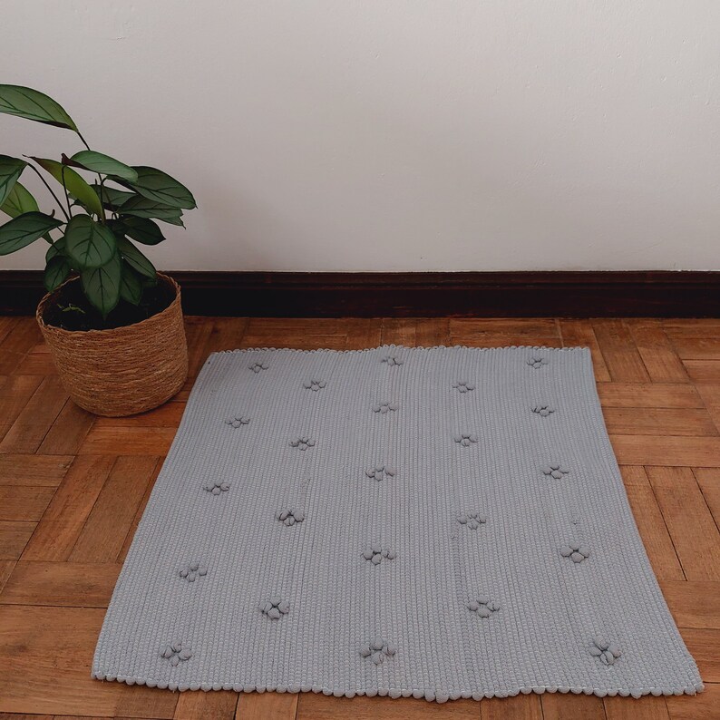 Puede incluir: Una alfombra gris claro con una superficie texturizada y un patr&oacute;n repetitivo de peque&ntilde;os c&iacute;rculos en relieve. La alfombra est&aacute; sobre un suelo de madera.
