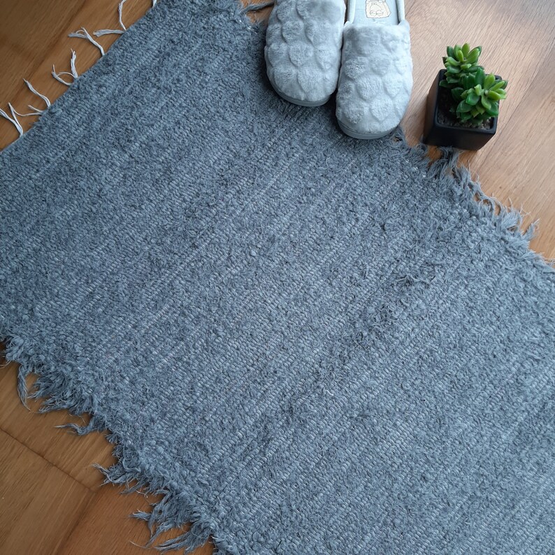 May include: A gray, fuzzy rug with a frayed edge. Two gray slippers are on top of the rug.