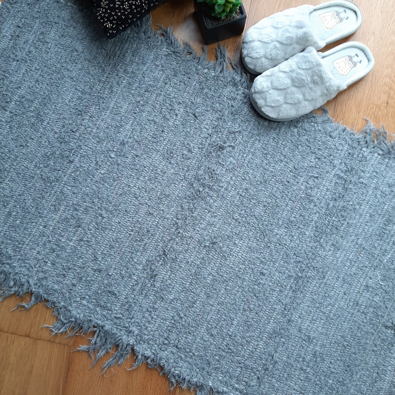 May include: A gray, fluffy rug with a frayed edge. The rug is made of a soft, textured material and has a subtle pattern.