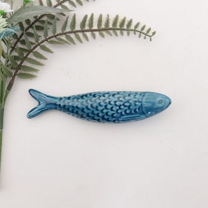 Puede incluir: Una figurita de pescado de cer&aacute;mica azul con un patr&oacute;n de escamas detallado. El pez es un objeto decorativo para el hogar o la oficina.