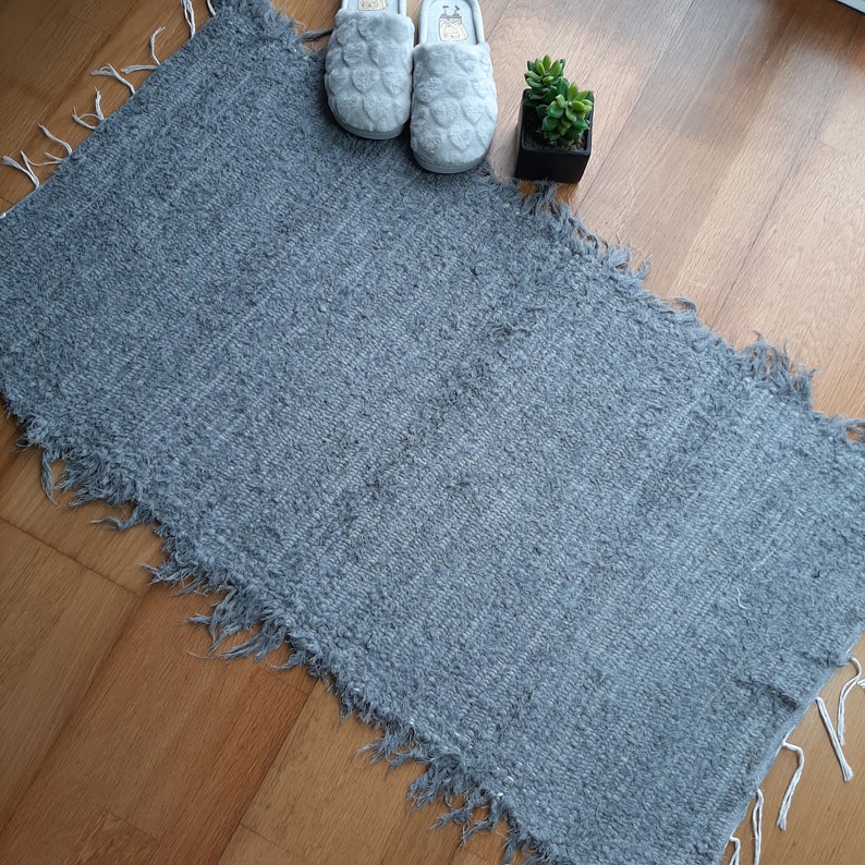May include: A gray, fluffy rug with frayed edges. The rug is on a wooden floor.