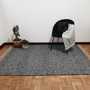 May include: A black and white patterned rug with a black chair and a potted plant in the background.