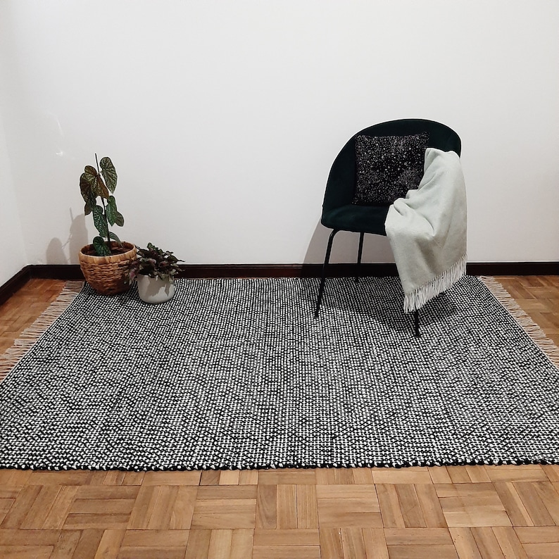 May include: A black and white patterned rug with a black chair and a potted plant in the background.