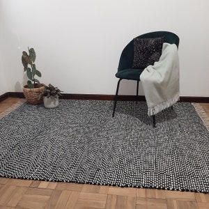 May include: A black and white patterned rug with a green chair and a throw blanket on it. The chair has a black cushion and a white pillow. There are two plants in pots on the rug.