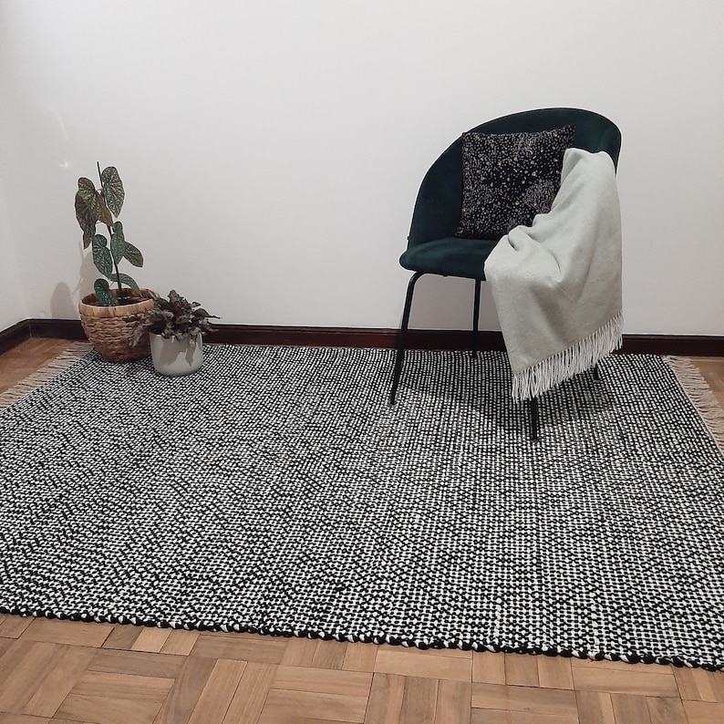 May include: A black and white patterned rug with a green chair and a throw blanket on it. The chair has a black cushion and a white pillow. There are two plants in pots on the rug.