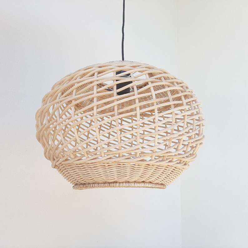 May include: A round, woven wicker pendant light fixture with a natural beige color. The light fixture is hanging from a black cord.