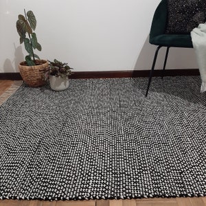 May include: Black and white geometric patterned rug with a woven texture. The rug is laid out on a wooden floor.
