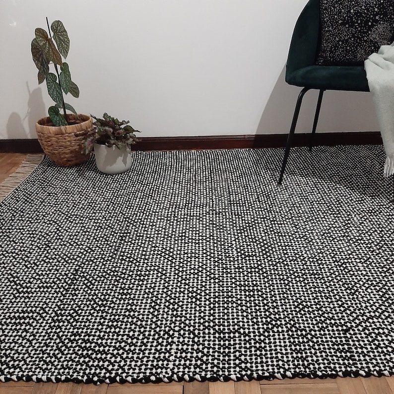 May include: Black and white geometric patterned rug with a woven texture. The rug is laid out on a wooden floor.