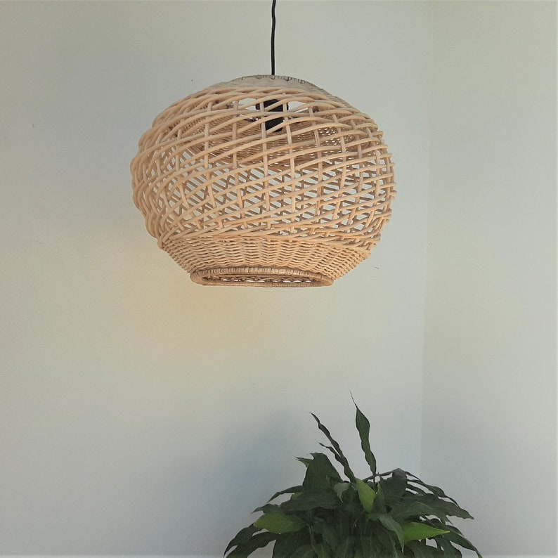 May include: A round, woven wicker pendant light fixture hangs from a black cord against a white wall.