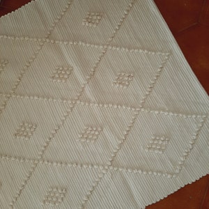May include: A white woven rug with a diamond pattern. The rug has a textured surface with raised bumps.