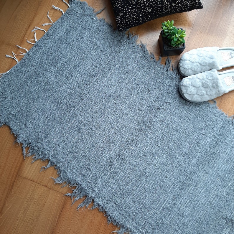 May include: A gray, fluffy rug with frayed edges. The rug is laid out on a wooden floor.