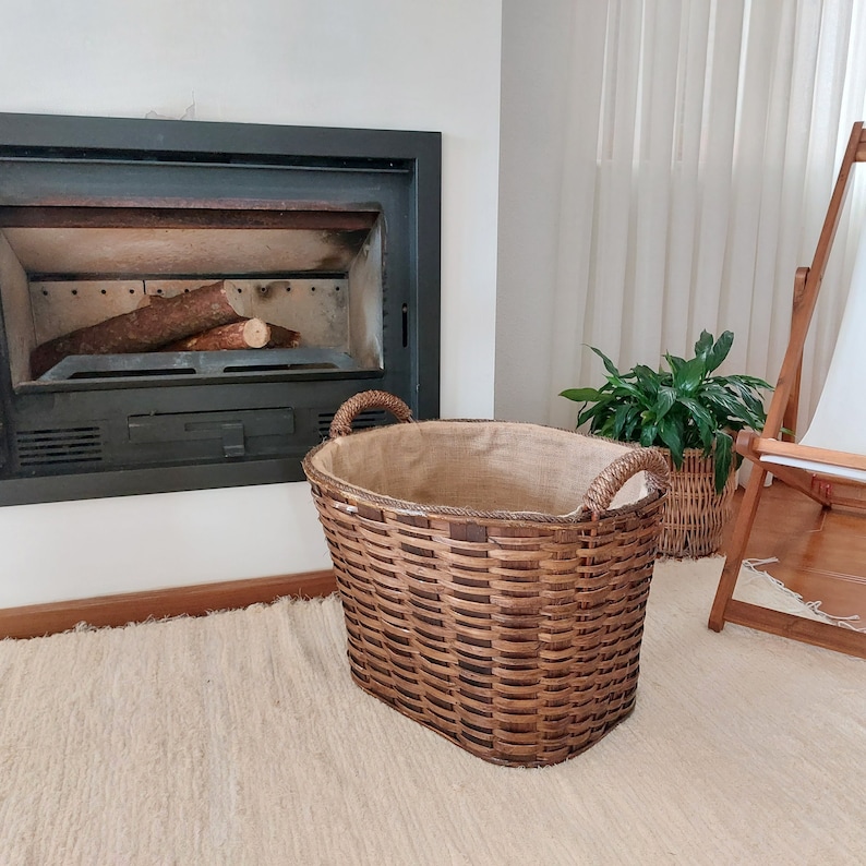 May include: A large, brown woven basket with two curved handles. The basket has a rectangular shape and is lined with a tan fabric. It is designed for storing firewood near a fireplace.
