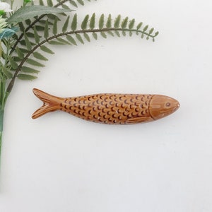 Puede incluir: Una figurita de pescado de cer&aacute;mica marr&oacute;n en forma de sardina. El pez tiene un patr&oacute;n de escamas detallado y una boca ligeramente hacia arriba.