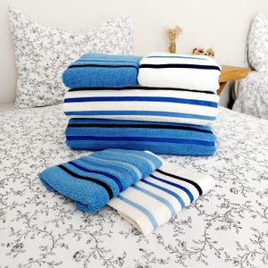 May include: A collection of blue and white striped towels, alongside solid blue ones, neatly stacked on a bed. The bed features a floral patterned duvet and pillow. The towels have black stripes.