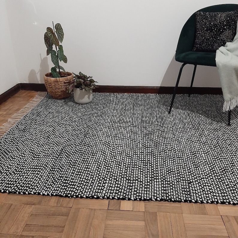 May include: A black and white patterned rug with a fringe border. The rug is made of a woven material and has a textured surface.