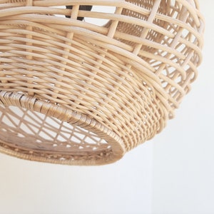 May include: A natural woven wicker pendant light fixture with a round shape. The light fixture is made of light brown wicker and has a woven pattern.