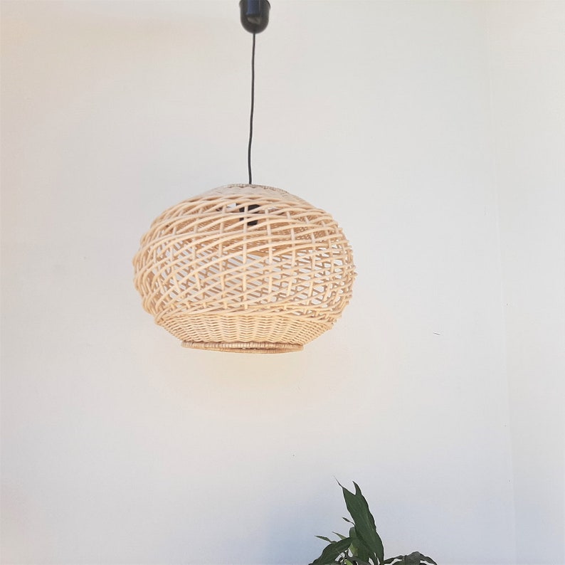 May include: A round, natural woven wicker pendant light fixture hangs from a black cord against a white wall.