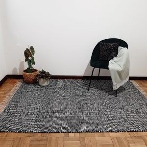 May include: A black and white patterned rug with a black chair and a green plant in a wicker basket.