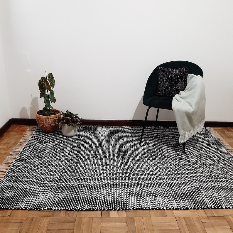 May include: A black and white patterned rug with a black chair and a green plant in a wicker basket.