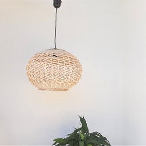 May include: A round, woven wicker pendant light fixture hangs from a black cord against a white wall.