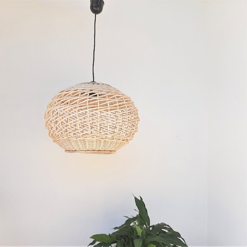 May include: A round, woven wicker pendant light fixture hangs from a black cord against a white wall.