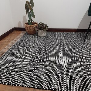 May include: Black and white checkered rug with a woven texture. The rug is made of natural fibers and has a simple, modern design.