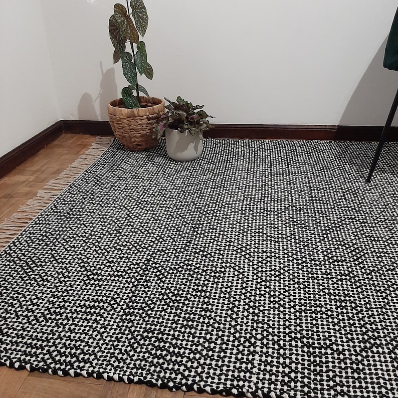 May include: Black and white checkered rug with a woven texture. The rug is made of natural fibers and has a simple, modern design.
