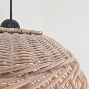 May include: A close-up of a woven wicker pendant light shade with a black cord and a black bulb. The shade is made of natural woven rattan and has a round shape.