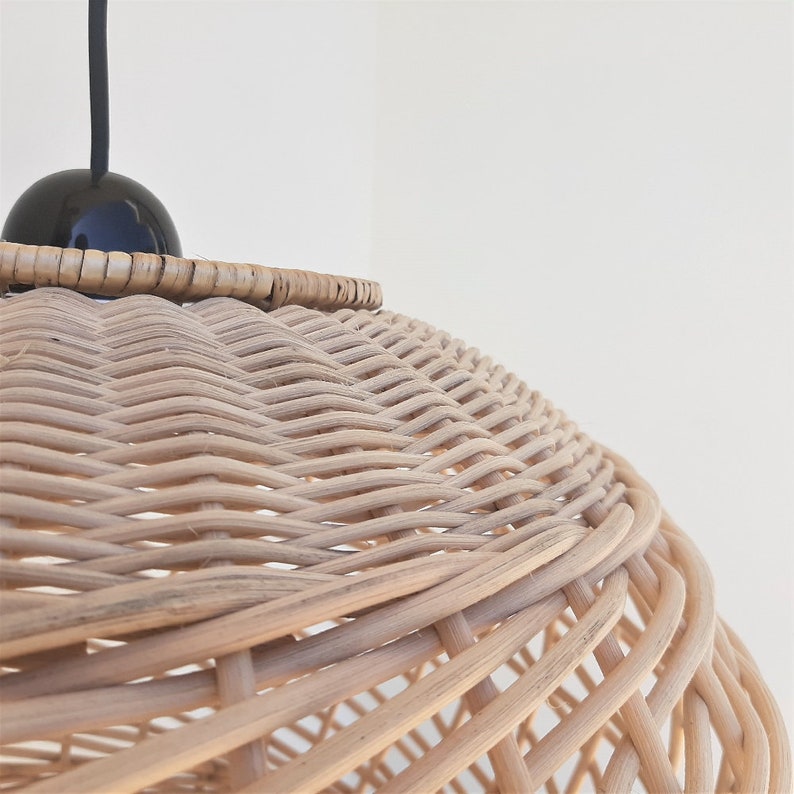 May include: A close-up of a woven wicker pendant light shade with a black cord and a black bulb. The shade is made of natural woven rattan and has a round shape.