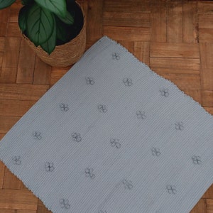 Puede incluir: Una alfombra de ba&ntilde;o azul claro con un peque&ntilde;o patr&oacute;n de flores. La alfombra tiene un borde festoneado.