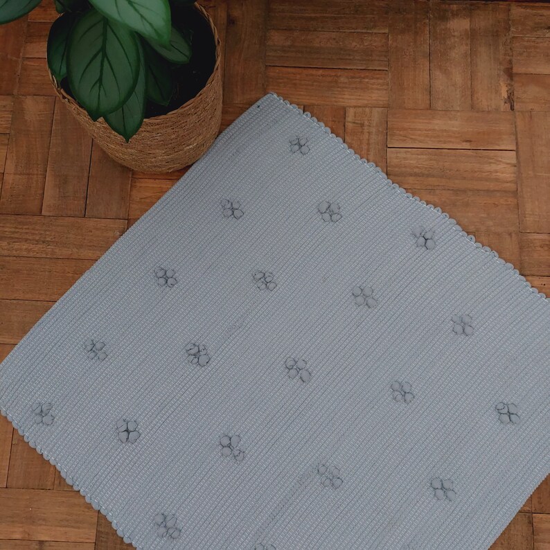 Puede incluir: Una alfombra de ba&ntilde;o azul claro con un peque&ntilde;o patr&oacute;n de flores. La alfombra tiene un borde festoneado.
