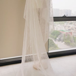 May include: A white lace bridal veil draped over a mannequin. The veil is long and flowing, with a delicate floral pattern.