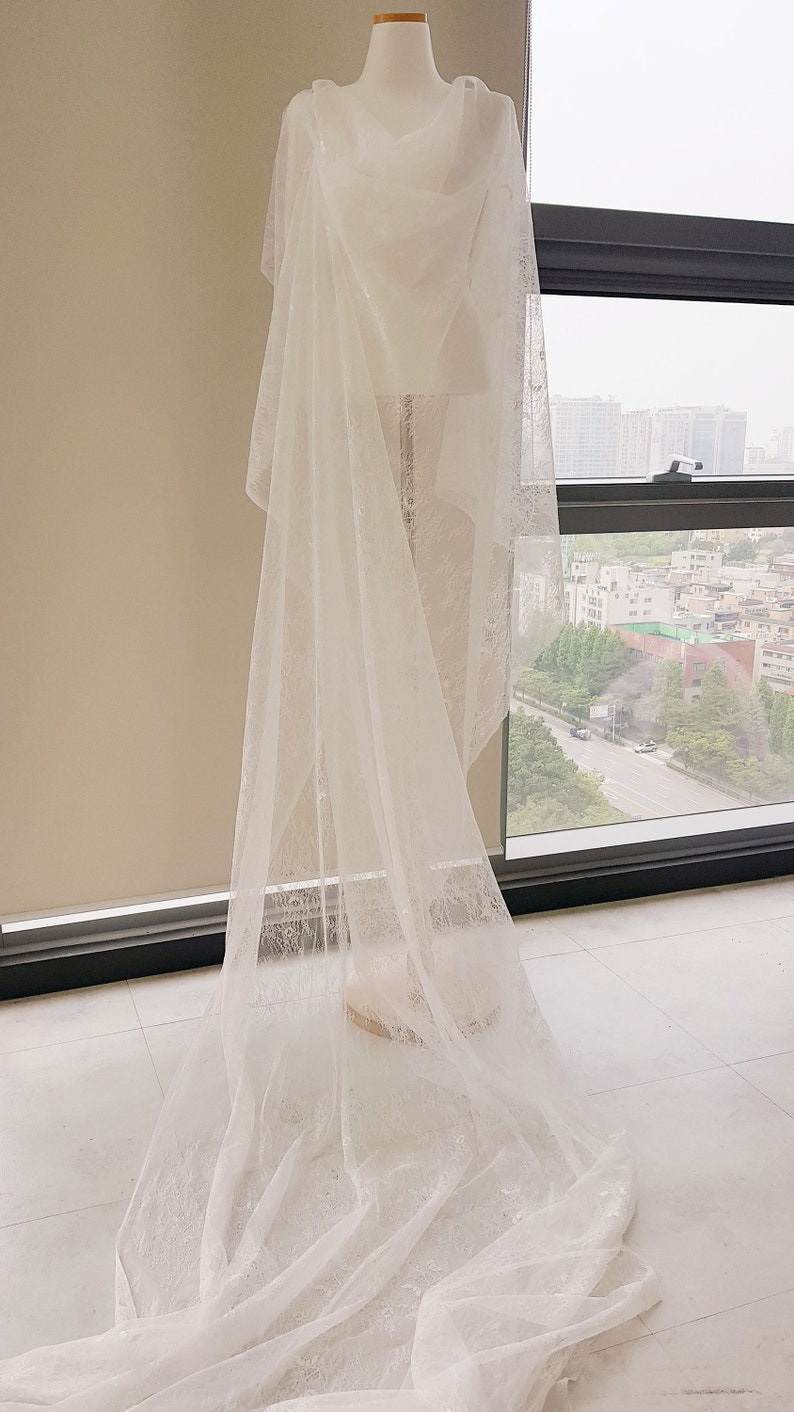 May include: A white lace bridal veil draped over a mannequin. The veil is long and flowing, with a delicate floral pattern.