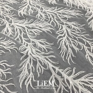 May include: White beaded lace fabric with a delicate floral pattern. The fabric is sheer and has a soft, flowing texture.