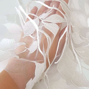 Puede incluir: Tela de encaje floral blanca con un patr&oacute;n delicado. El encaje es transparente y tiene una textura suave y fluida.