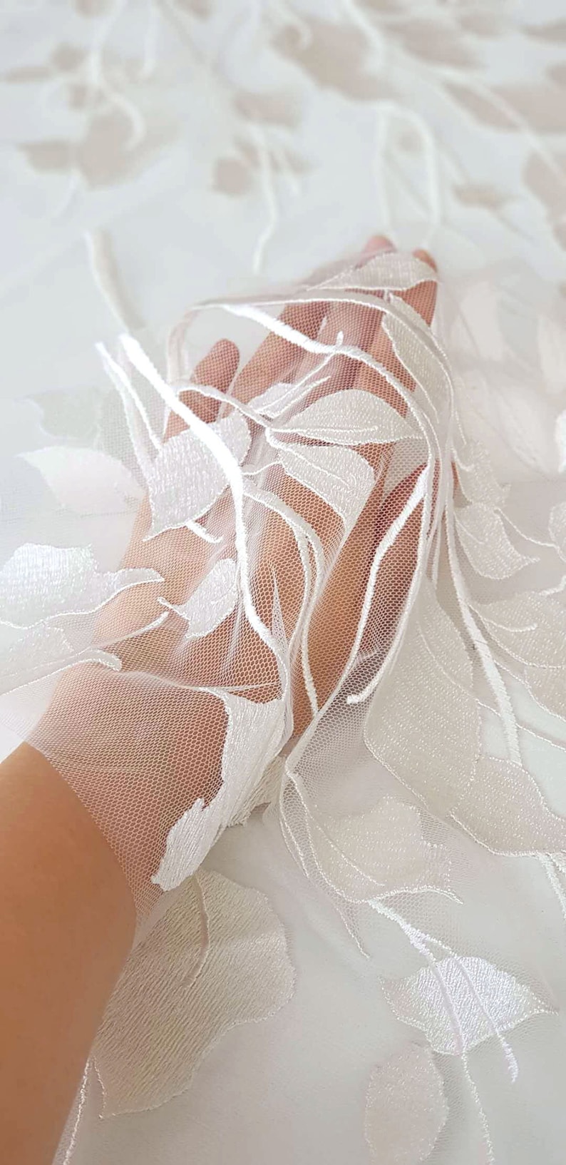 Puede incluir: Tela de encaje floral blanca con un patr&oacute;n delicado. El encaje es transparente y tiene una textura suave y fluida.