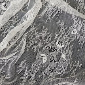 May include: White lace fabric with a delicate floral pattern. The lace is sheer and has a soft, flowing texture.