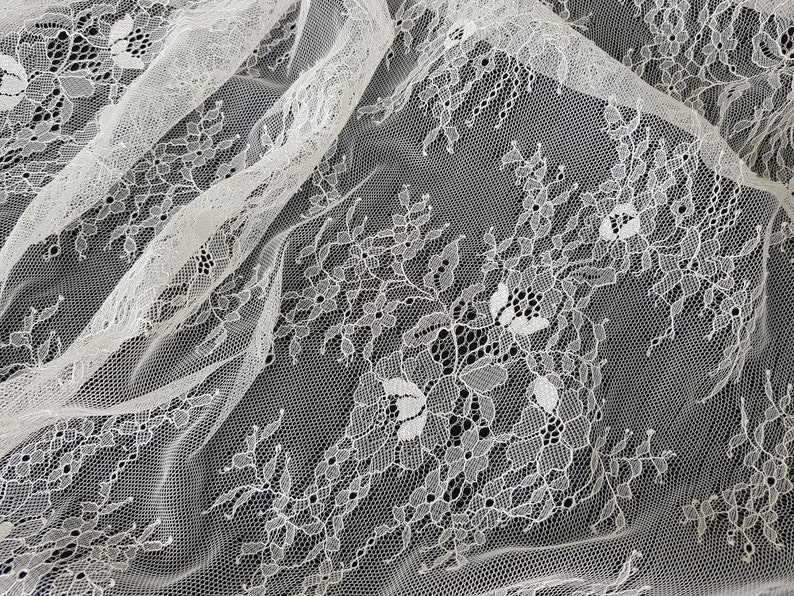 May include: White lace fabric with a delicate floral pattern. The lace is sheer and has a soft, flowing texture.