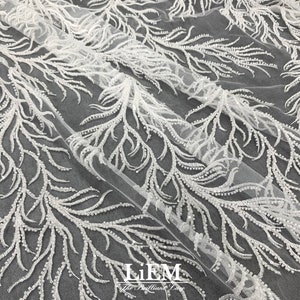 May include: White beaded lace fabric with a delicate feather design. The fabric is sheer and has a soft, flowing texture. The beads are small and evenly spaced, creating a subtle shimmer.