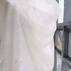 May include: White lace fabric with a delicate floral pattern. The fabric is draped over a white mannequin.