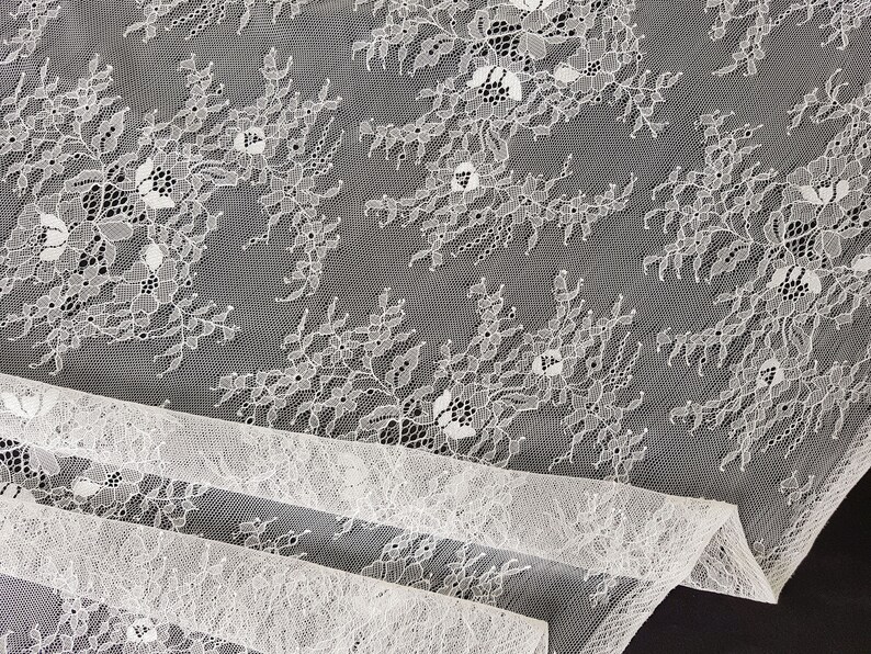 May include: White lace fabric with a delicate floral pattern. The lace is soft and sheer, and it has a subtle shimmer.