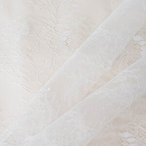 May include: White lace fabric with a delicate floral pattern. The fabric is sheer and has a soft, flowing texture.