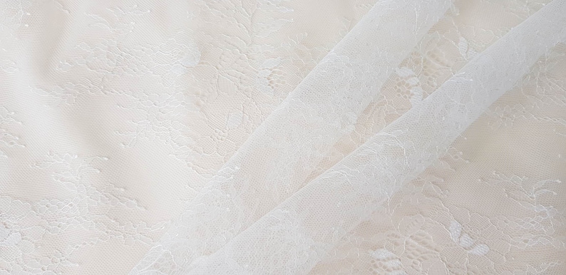 May include: White lace fabric with a delicate floral pattern. The fabric is sheer and has a soft, flowing texture.