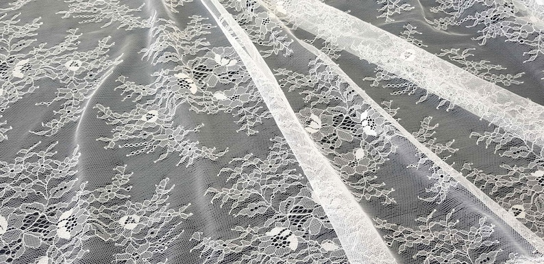 May include: White lace fabric with a floral pattern. The lace is delicate and has a soft, flowing texture.