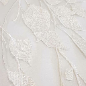 Puede incluir: Tela de encaje blanca con un delicado patr&oacute;n floral. La tela es transparente y tiene una textura suave y fluida.