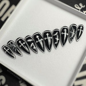 May include: Set of ten black and white press-on nails with different designs. The designs include crosses, bats, and spiderwebs.